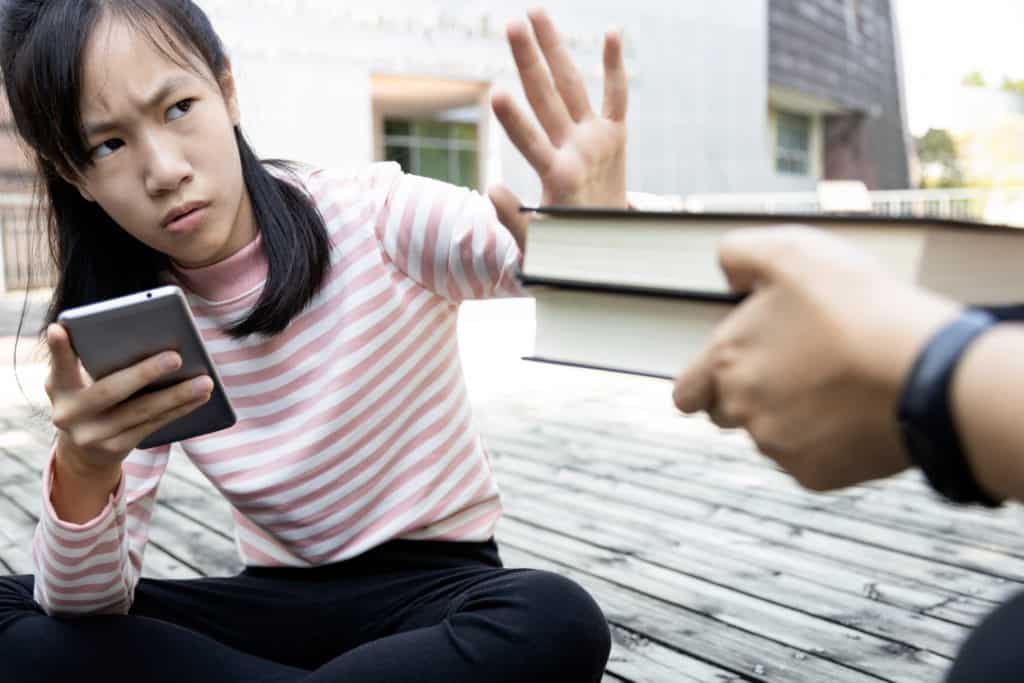 girl looking at cell phone holding up hand to refuse a stack of books to lead the blog about motivation issues in older readers