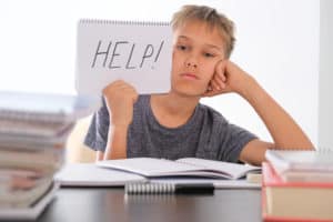 Upset boy sitting at the table, doing his homework among pile of books. Word Help is written on open notebook. Learning difficulties, school, education concept to head blog 5 ways to help middle school readers