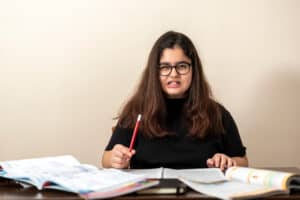 frustrated girl in black shirt holding pencil over books used as cover photo on blog with four steps to scaffold written response